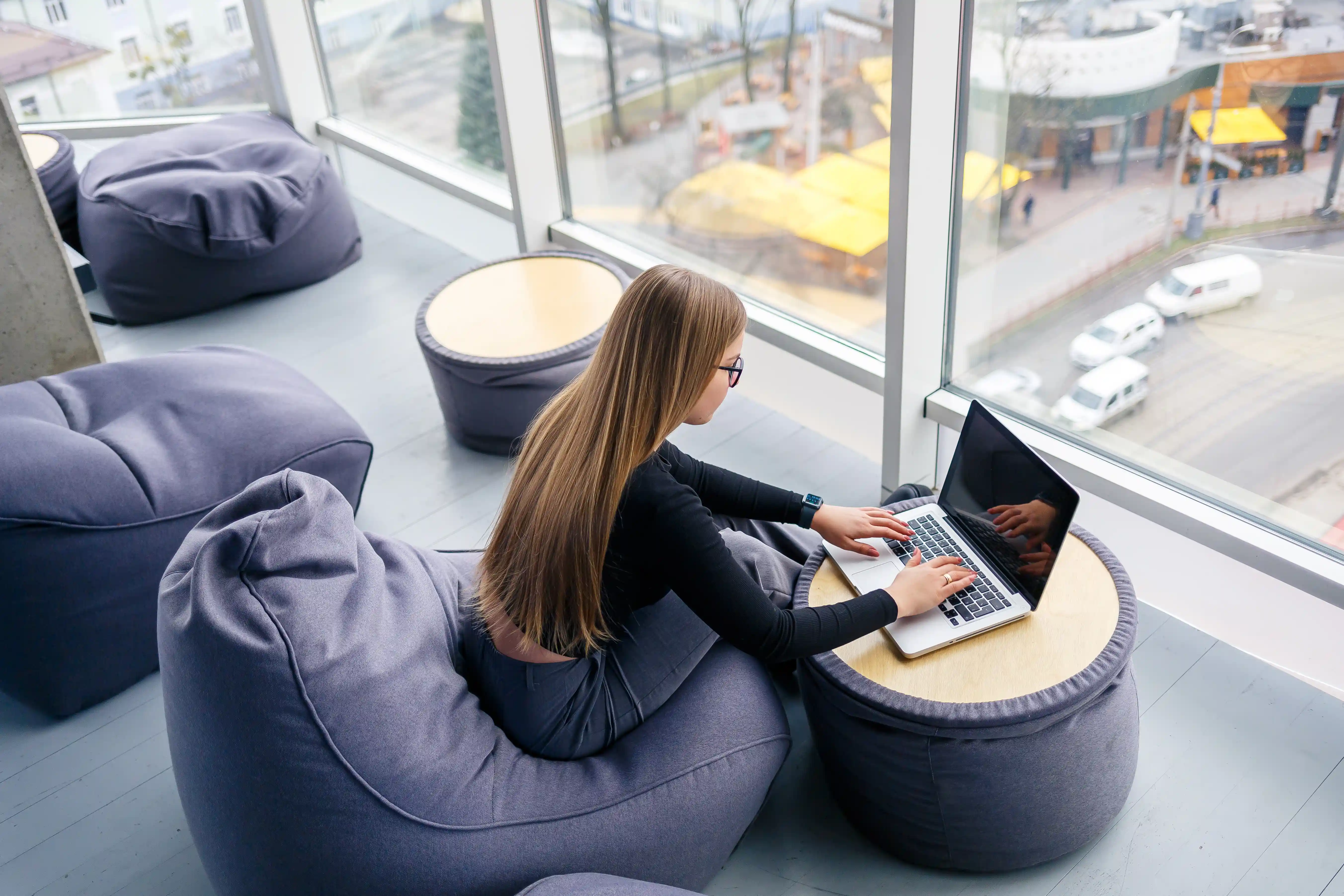 beautiful-young-woman-manager-sits-with-laptop-soft-pouf-near-panoramic-window-girl-businessman-working-new-project